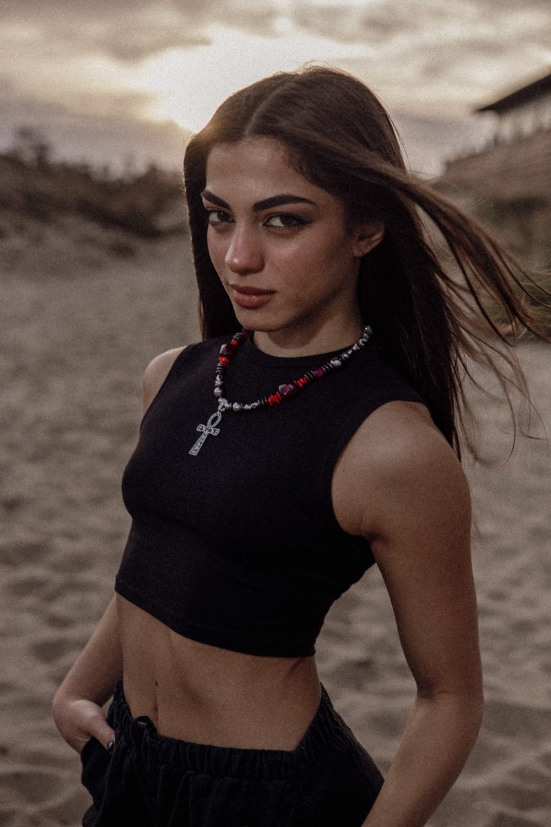 Ragazza in top nero sulla sabbia al tramonto con la collana ANKH — SCARLET: perline rosse e nere e ciondolo ankh