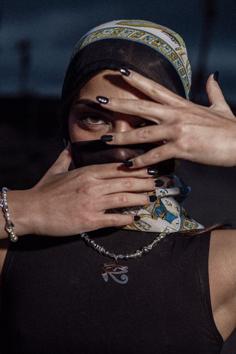Mani con smalto nero davanti al viso e un foulard a motivi egizi; al collo la collana HORUS — SILVER con l'Occhio di Horus argentato