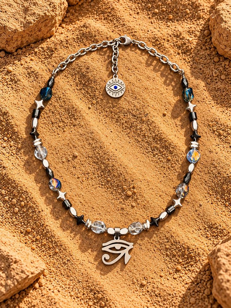 Collana MALOCCHIO «HORUS — MIRAGE»: perle trasparenti e iridescenti, stelline e Occhio di Horus argentato, sulla sabbia
