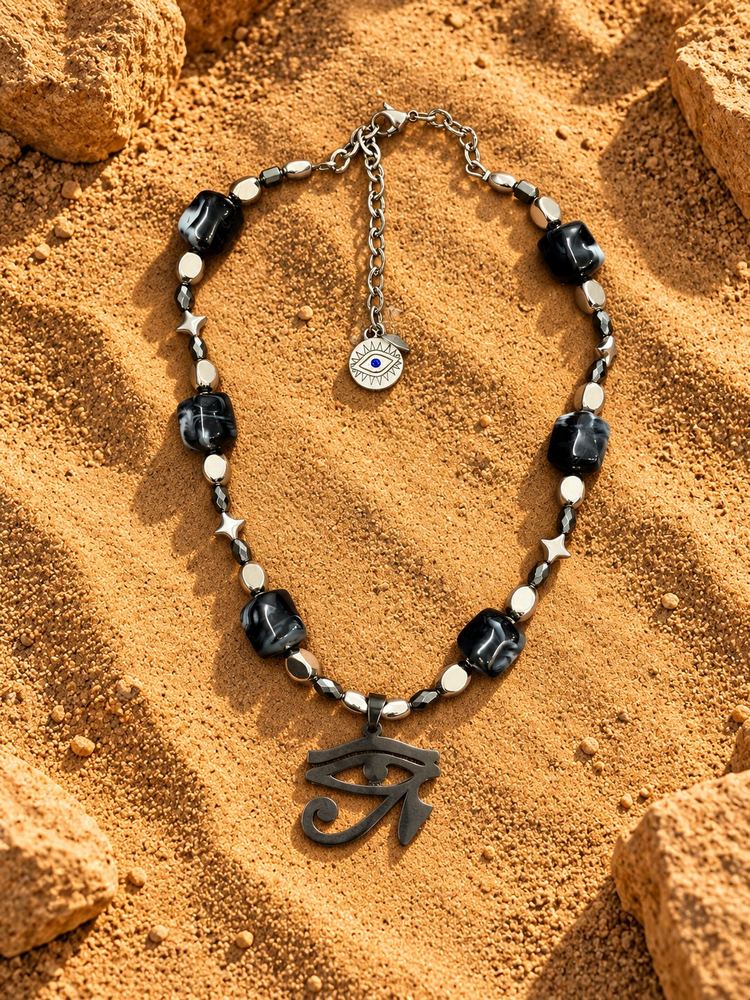 Collana MALOCCHIO «HORUS — ONYX»: perle nere marmorizzate, stelline argentate e Occhio di Horus nero, sulla sabbia